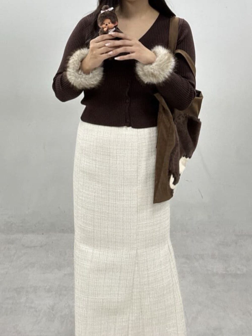 ホワイト系のスカート、ブラウン系のカーディガン/ボレロ、ブラウン系のトートバッグを着用したレディースの冬コーディネートの3枚目の写真