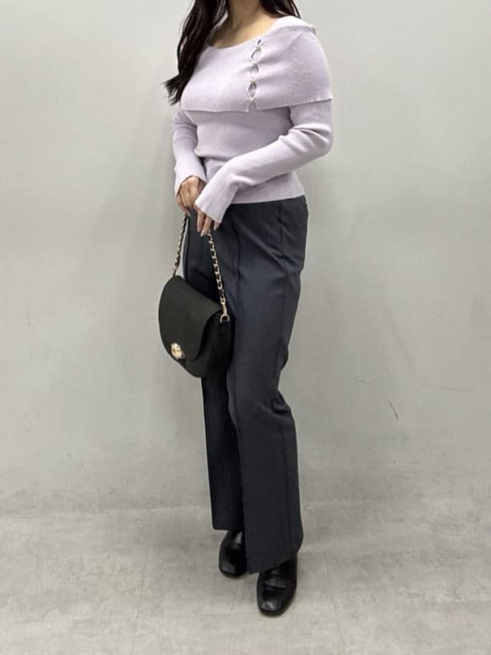 グレー系のスラックス、ブラック系のショルダーバッグ、パープル系のニット/セーターを着用したレディースの冬コーディネートの2枚目の写真