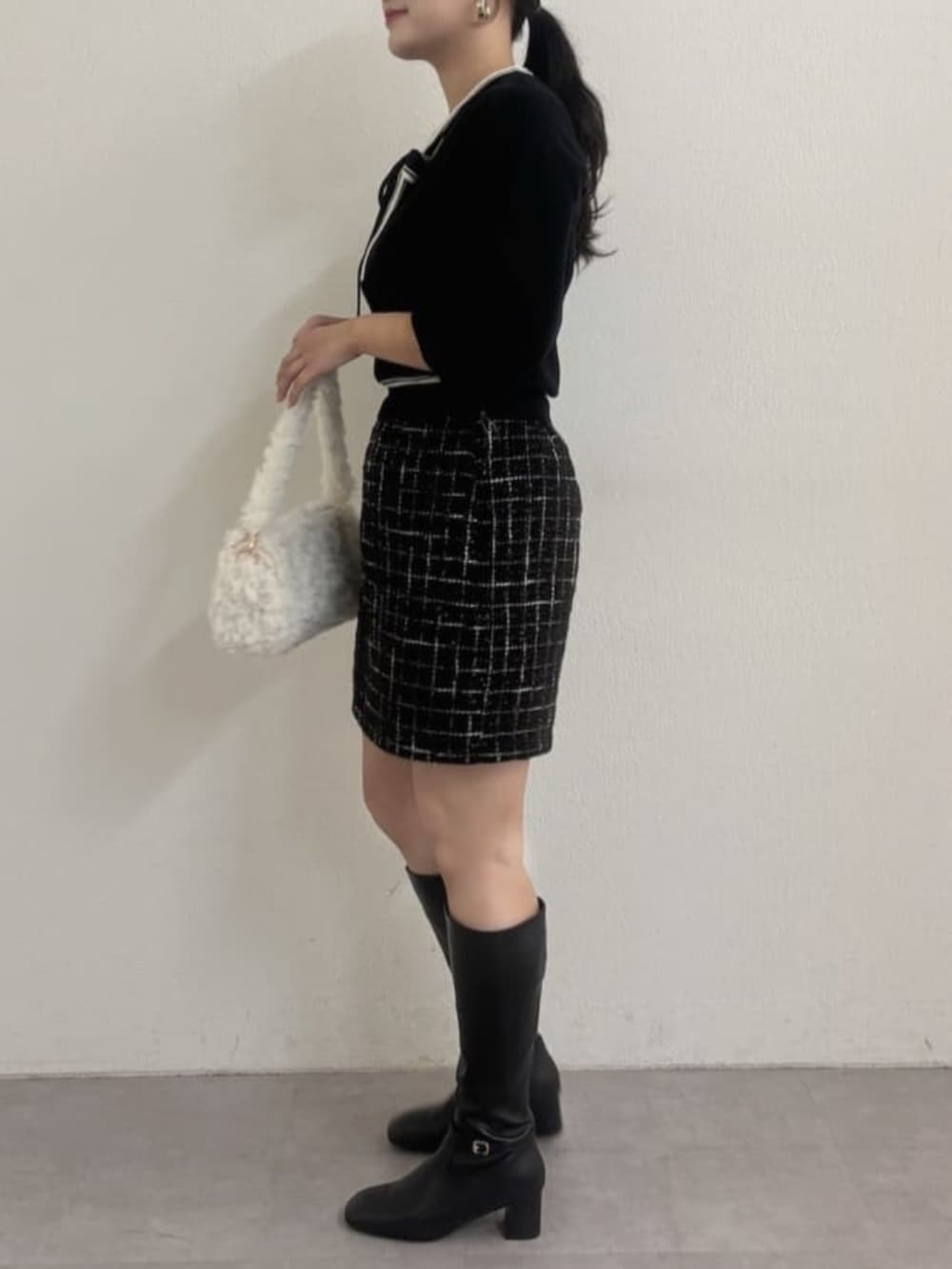 ブラック系のブーツ、ブラック系のスカート、ホワイト系のハンドバッグを着用したレディースの秋コーディネートの2枚目の写真