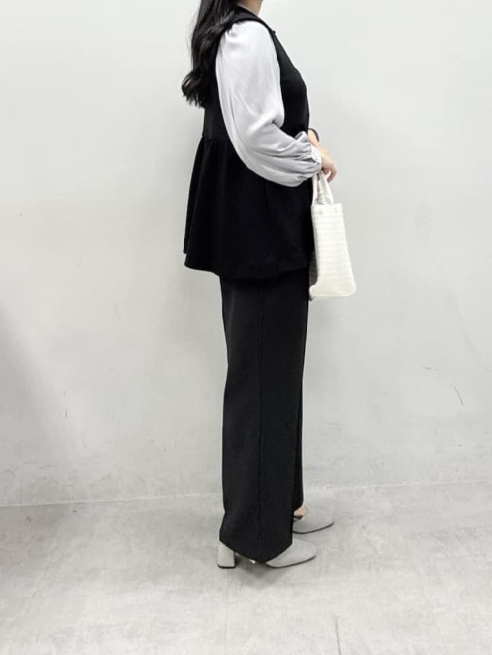 ホワイト系のハンドバッグ、グレー系のサンダル、ブラック系のスラックスを着用したレディースの冬コーディネートの2枚目の写真