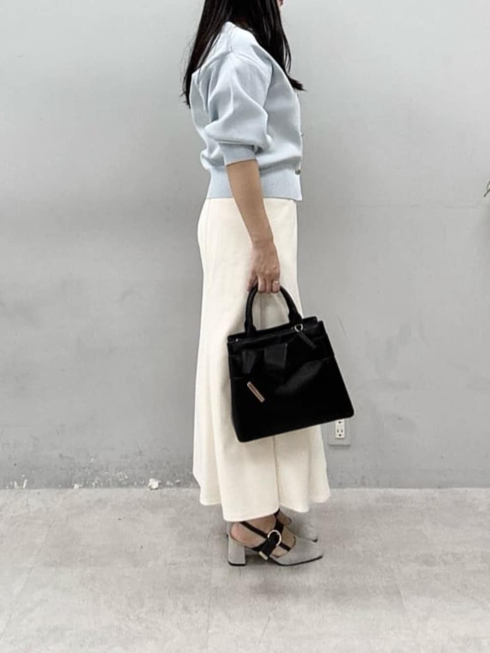 ブラック系のショルダーバッグ、ホワイト系のスカート、ブルー系のカーディガン/ボレロを着用したレディースの春コーディネートの2枚目の写真