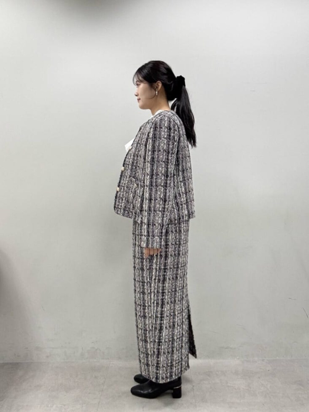 グレー系のスカート、グレー系のノーカラージャケット、ブラック系のブーツを着用したレディースの秋コーディネートの6枚目の写真