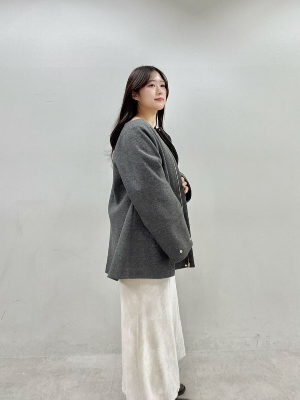 グレー系のノーカラーコート、ホワイト系のスカート、グレー系のニット/セーターを着用したレディースの秋コーディネートの2枚目の写真