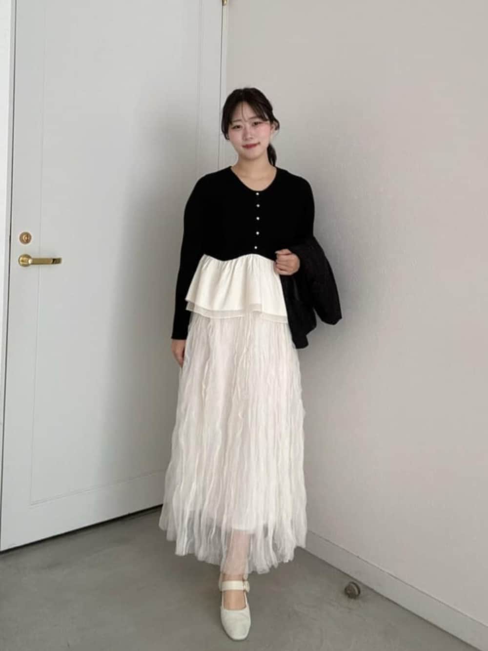 ブラック系のニット/セーター、ホワイト系のスカートを着用したレディースの冬コーディネートの2枚目の写真