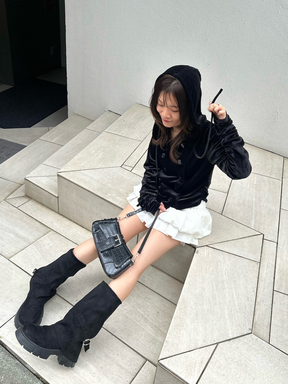 ブラック系のパーカー、ホワイト系のスカート、ブラック系のブーツを着用したレディースの秋コーディネートの6枚目の写真