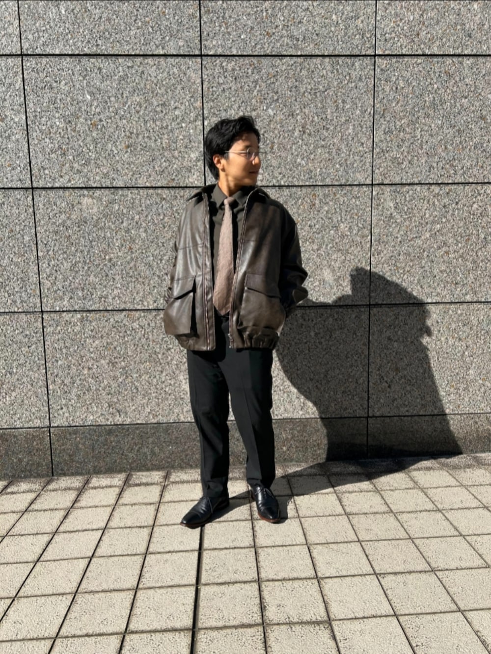 ブラウン系のブルゾン、ベージュ系のネクタイ、ブラック系のスラックスを着用したメンズの秋コーディネートの2枚目の写真