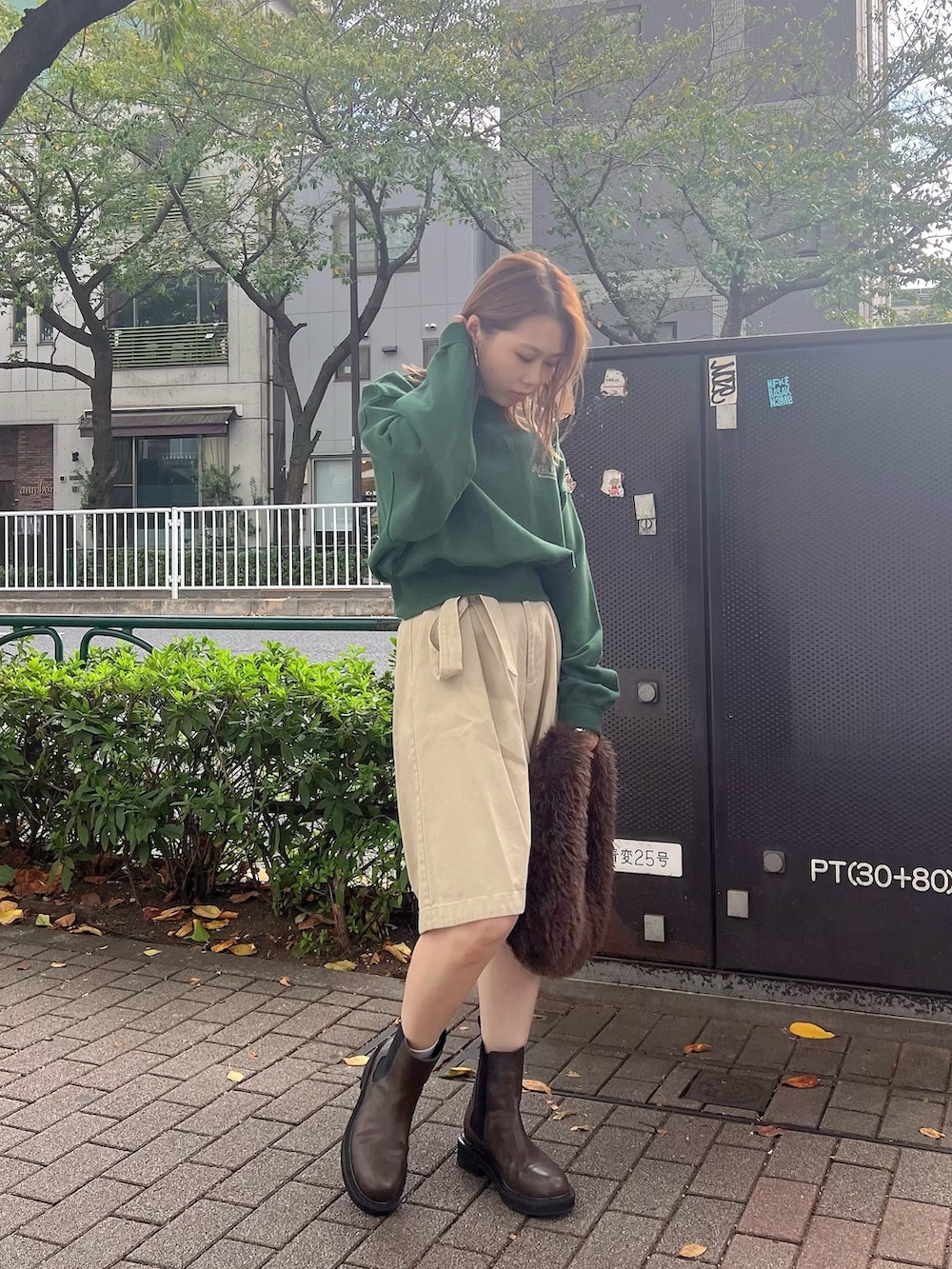 グリーン系のスウェット、ベージュ系のチノパンツ、ブラウン系のハンドバッグを着用したレディースの秋コーディネートの2枚目の写真