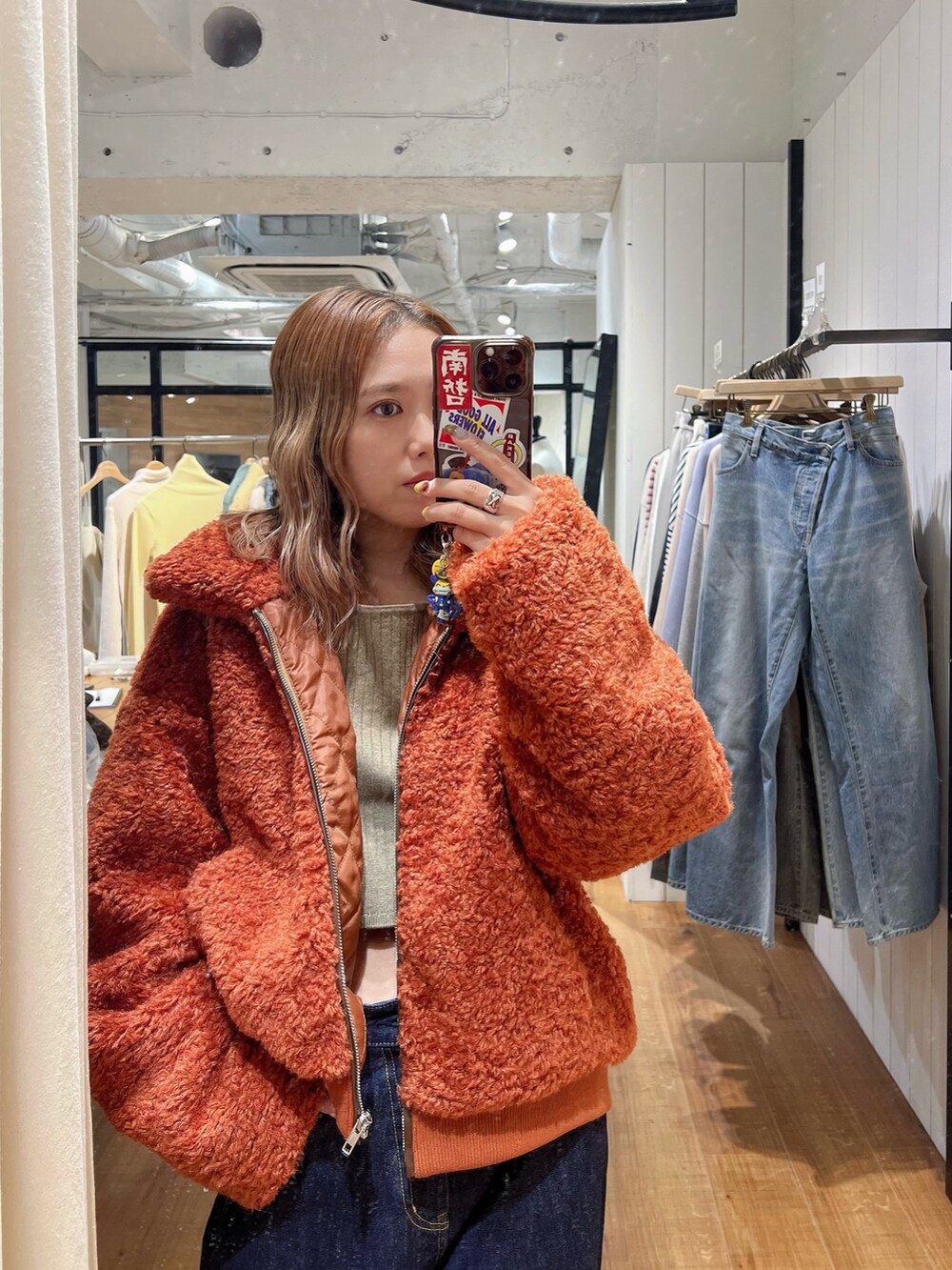 オレンジ系のブルゾン、グレー系のニット/セーター、ブルー系のデニムパンツを着用したレディースの冬コーディネートの2枚目の写真