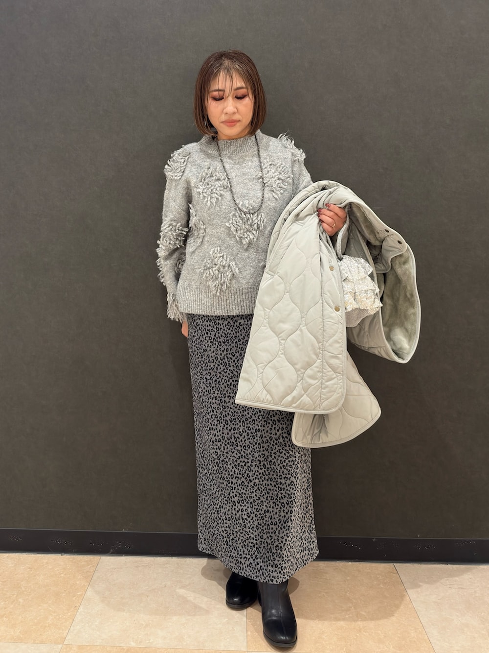 ブラック系のブーツ、シルバー系のショルダーバッグ、グレー系のスカートを着用したレディースの冬コーディネートの5枚目の写真