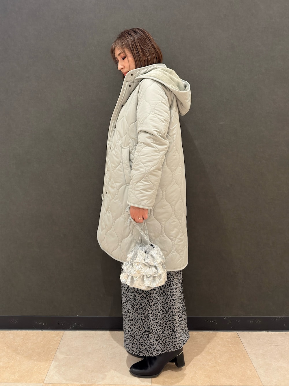 ブラック系のブーツ、シルバー系のショルダーバッグ、グレー系のスカートを着用したレディースの冬コーディネートの2枚目の写真