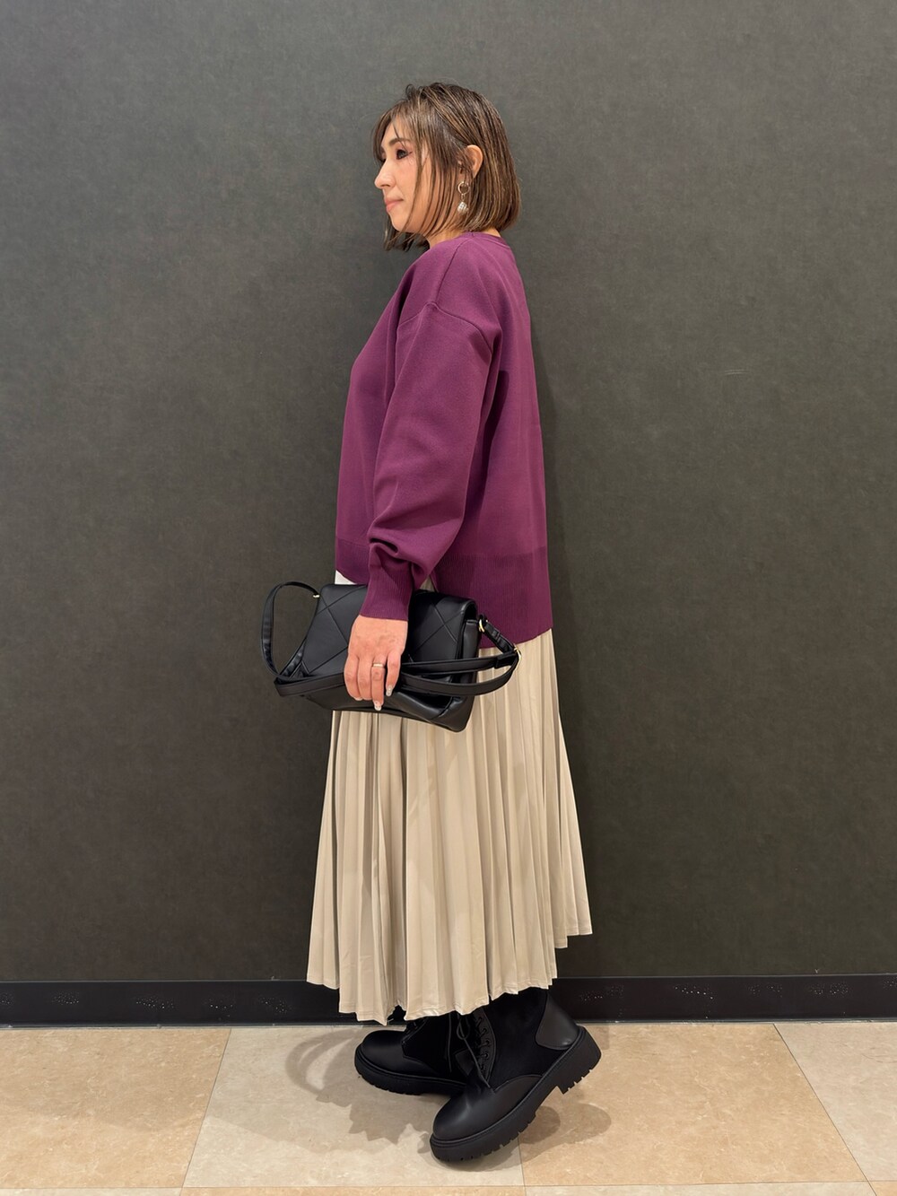 ブラック系のブーツ、ブラック系のショルダーバッグ、ベージュ系のスカートを着用したレディースの秋コーディネートの2枚目の写真