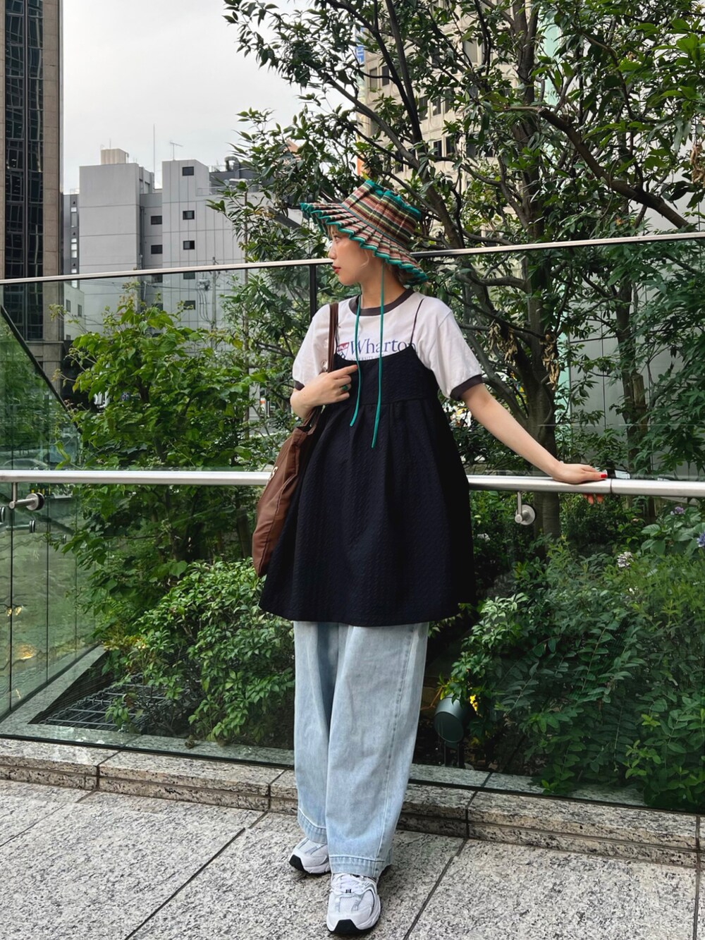 ブラウン系のトートバッグ、ブルー系のスラックス、ホワイト系のスニーカーを着用したレディースの夏コーディネートの2枚目の写真