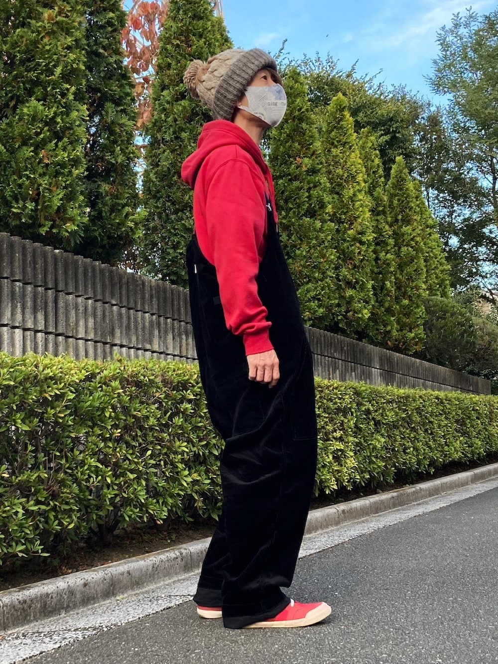 レッド系のスニーカー、ブラック系のサロペット/オーバーオール、レッド系のパーカーを着用したメンズの秋コーディネートの3枚目の写真