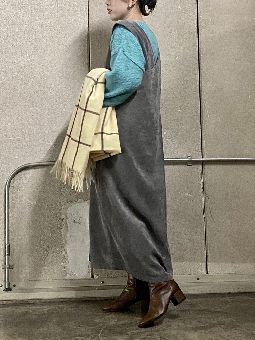 グレー系のジャンパースカート、ブラウン系のブーツ、ベージュ系のマフラーを着用したレディースの秋コーディネートの2枚目の写真