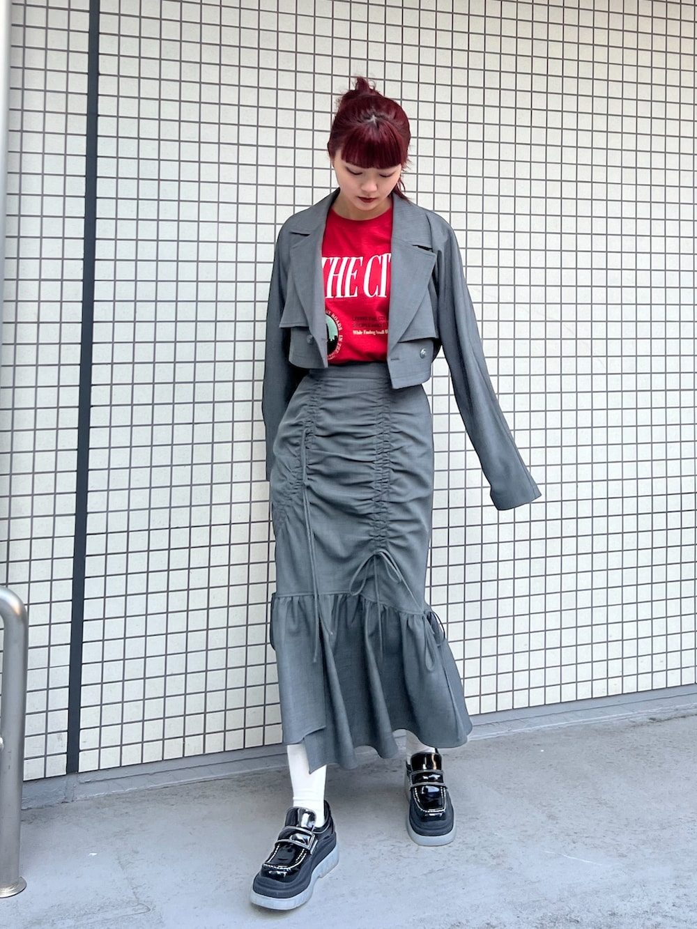 レッド系のTシャツ/カットソー、グレー系のトレンチコート、グレー系のスカートを着用したレディースの冬コーディネートの2枚目の写真