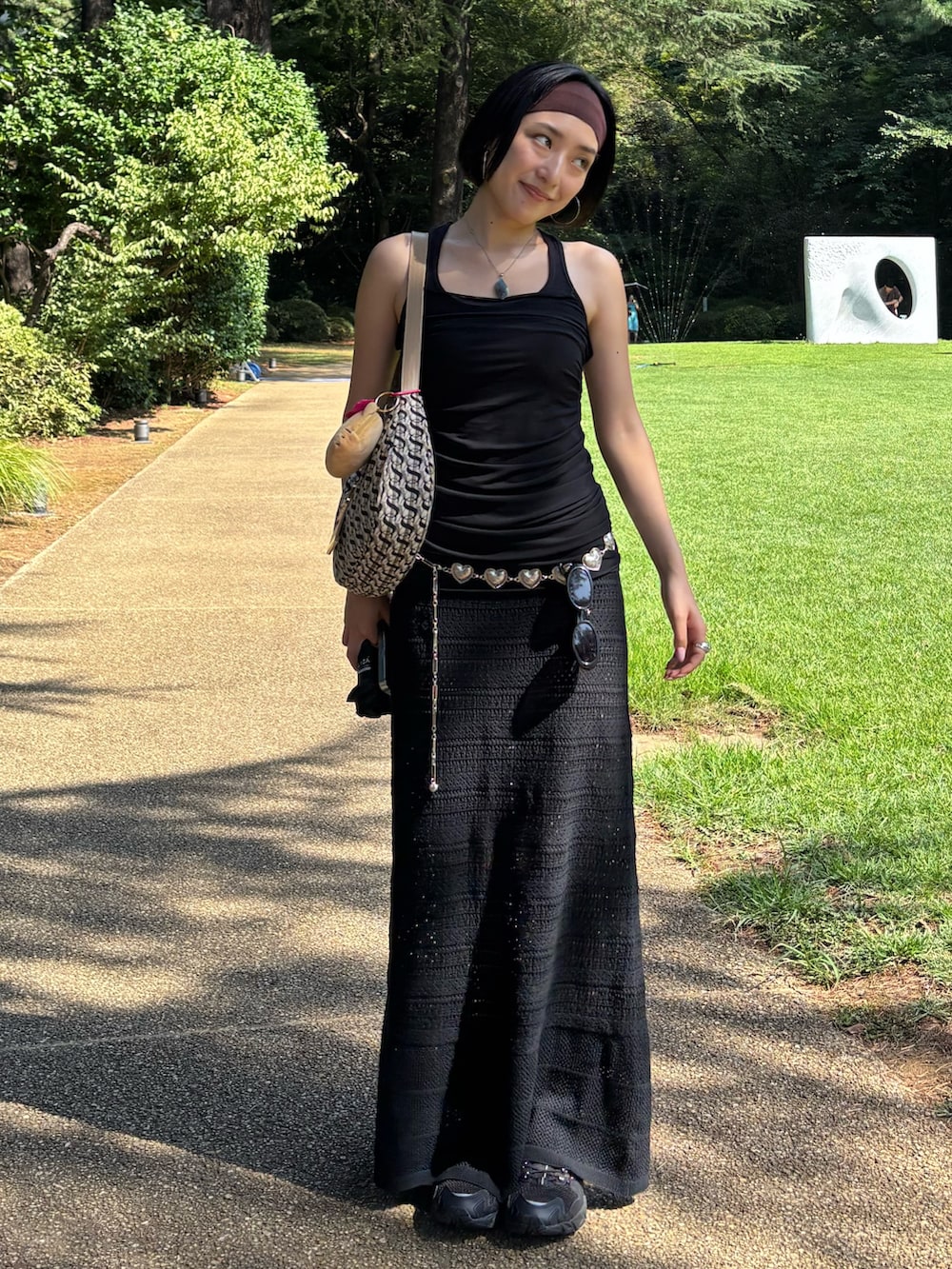 ベージュ系のハンドバッグ、ブラック系のスニーカー、ブラック系のタンクトップを着用したレディースの夏コーディネートの2枚目の写真