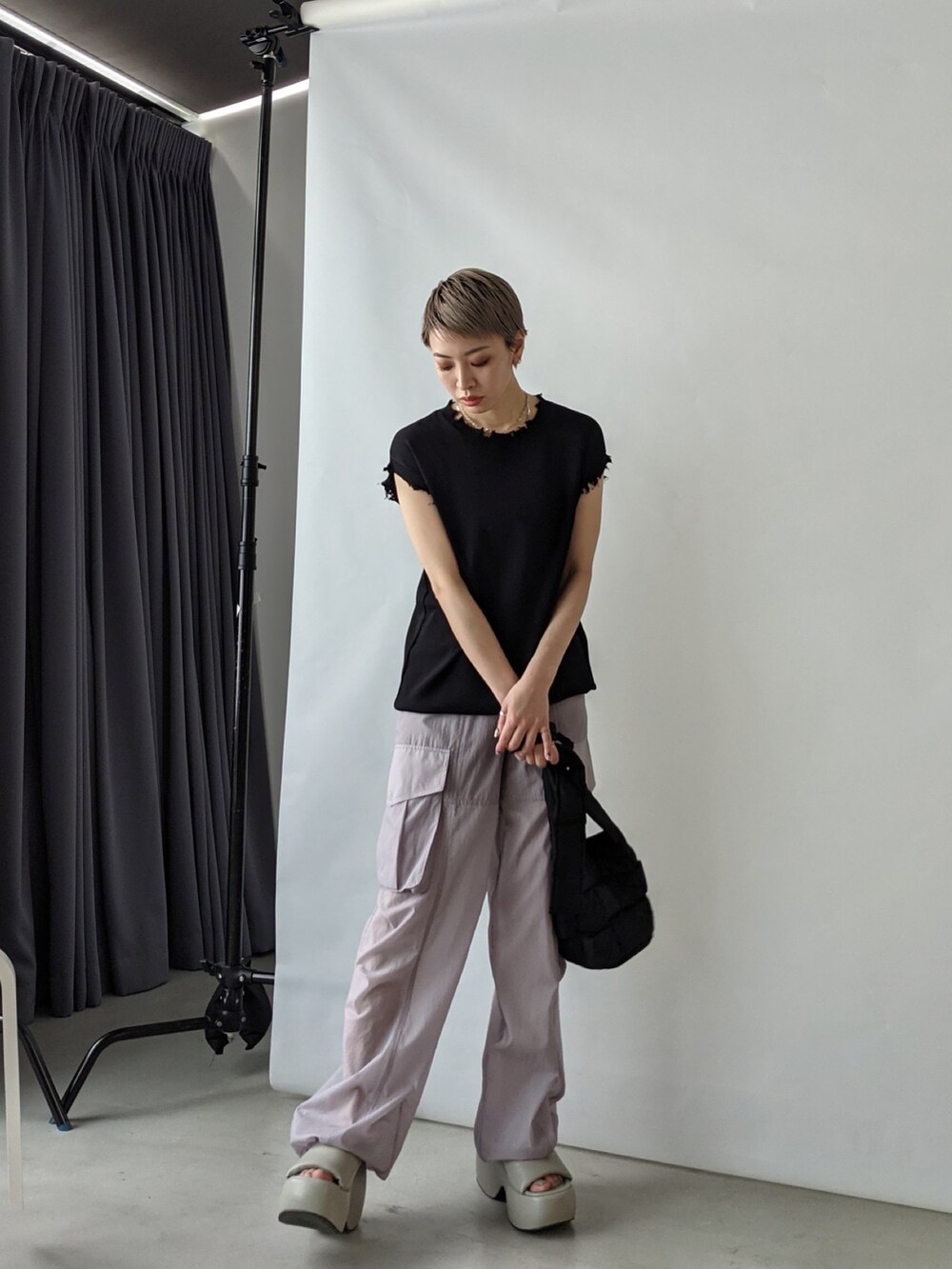 ブラック系のショルダーバッグ、ブラック系のニット/セーター、パープル系のスラックスを着用したレディースの春コーディネートの3枚目の写真