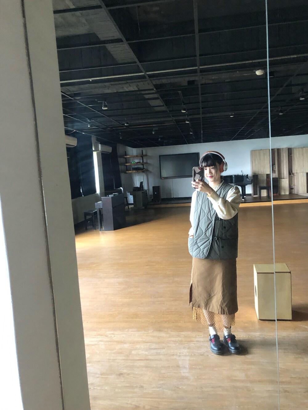 ブラック系のその他シューズ、オレンジ系のスカート、グリーン系のダウンベストを着用したレディースの冬コーディネートの2枚目の写真