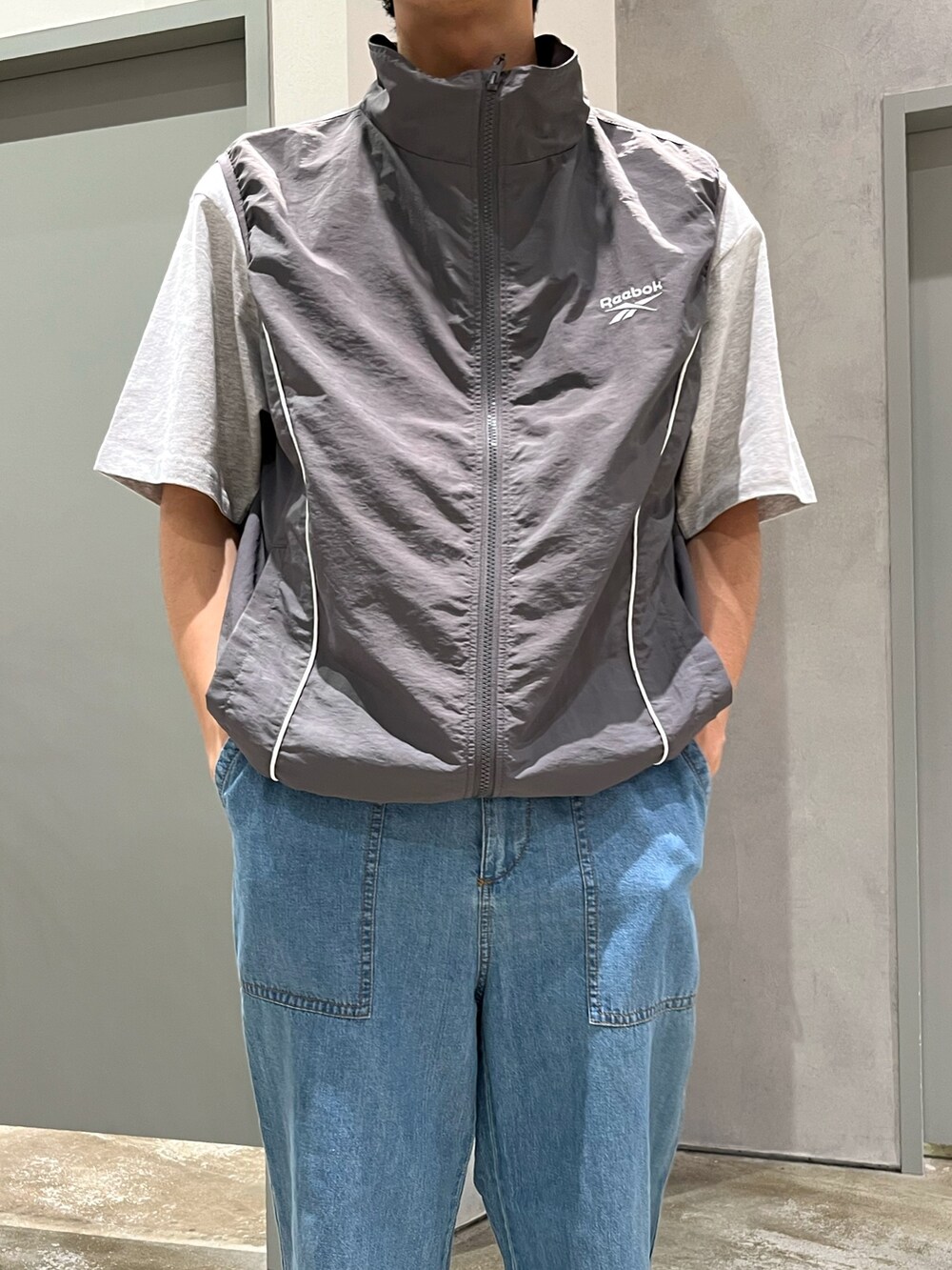 グレー系のベスト、ブラック系のスニーカー、ブルー系のデニムパンツを着用したメンズの夏コーディネートの3枚目の写真