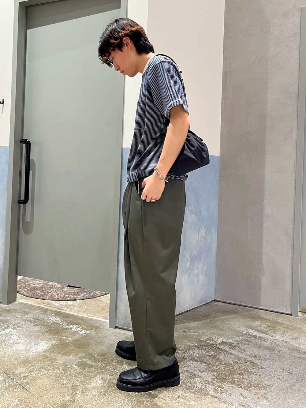 グリーン系のチノパンツ、ブルー系のTシャツ/カットソー、ブラック系のショルダーバッグを着用したメンズの夏コーディネートの2枚目の写真