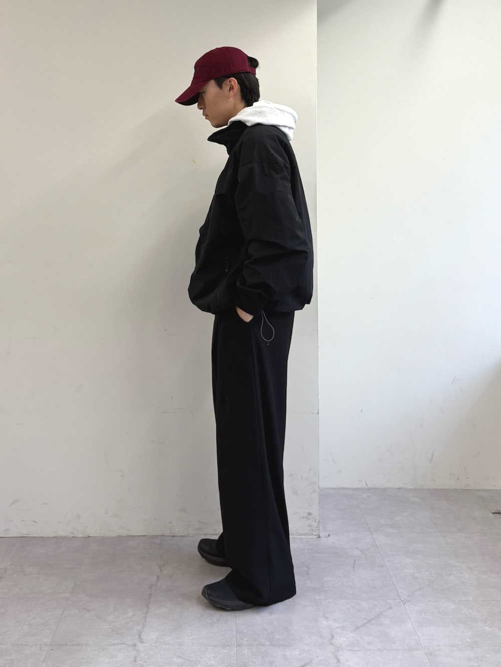 グレー系のパーカー、ブラック系のナイロンジャケット、ブラック系のスラックスを着用したメンズの春コーディネートの3枚目の写真