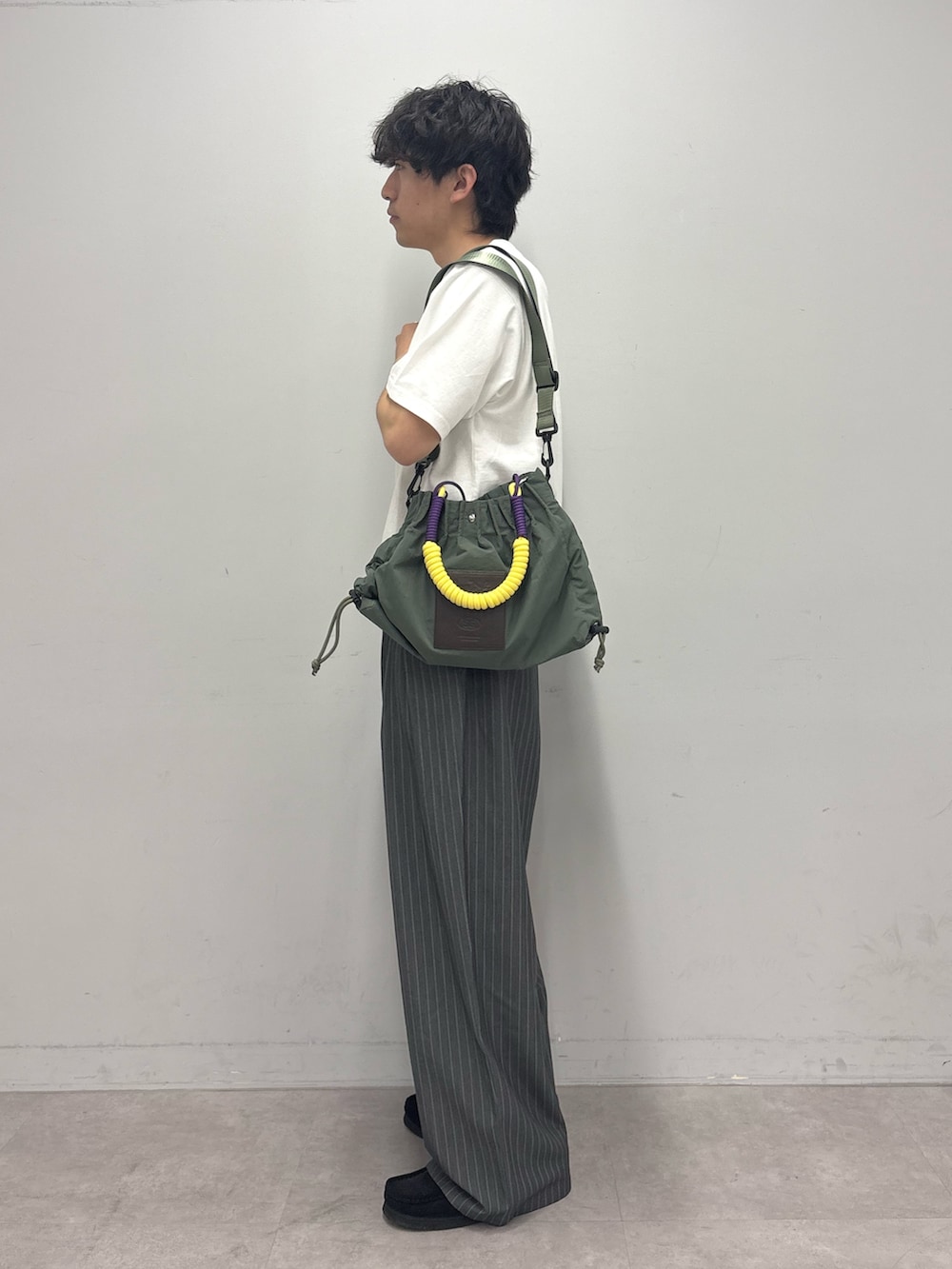 ホワイト系のTシャツ/カットソー、グリーン系のトートバッグ、グレー系のスラックスを着用したメンズの春コーディネートの2枚目の写真