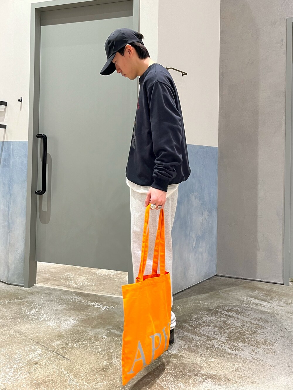 グレー系のスニーカー、グレー系のスウェットパンツ、オレンジ系のトートバッグを着用したメンズの春コーディネートの2枚目の写真