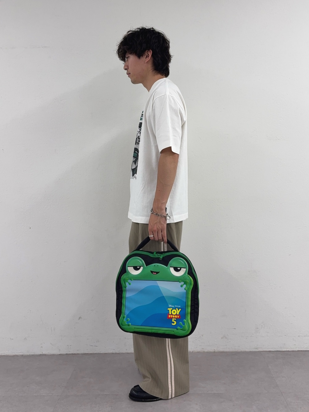 ホワイト系のTシャツ/カットソー、ベージュ系のスラックス、ブラック系のPC・タブレットケースを着用したメンズの春コーディネートの2枚目の写真