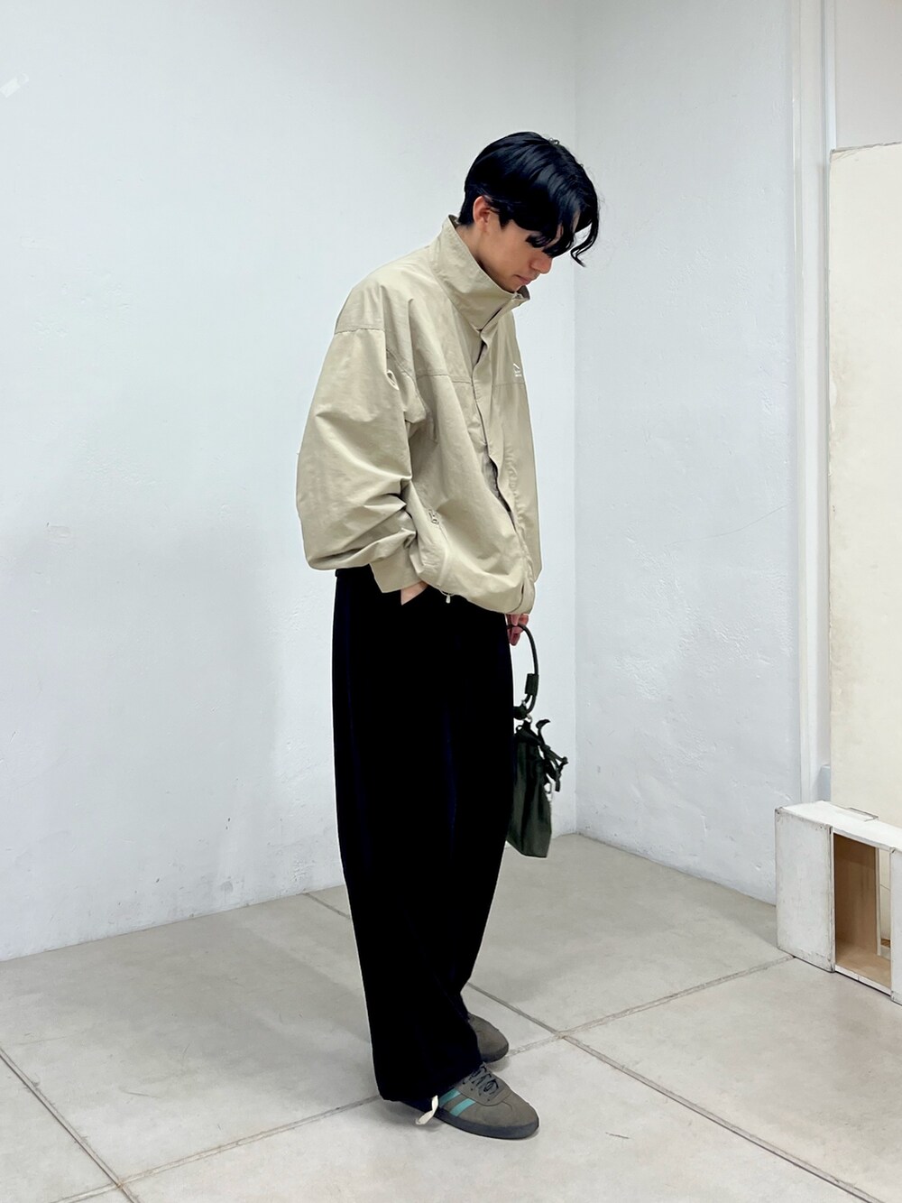 グレー系のナイロンジャケット、ブラック系のチノパンツ、グリーン系のショルダーバッグを着用したメンズの秋コーディネートの2枚目の写真