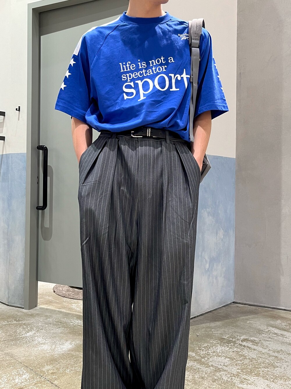 グレー系のスラックス、グレー系のスニーカー、ブルー系のTシャツ/カットソーを着用したメンズの夏コーディネートの3枚目の写真