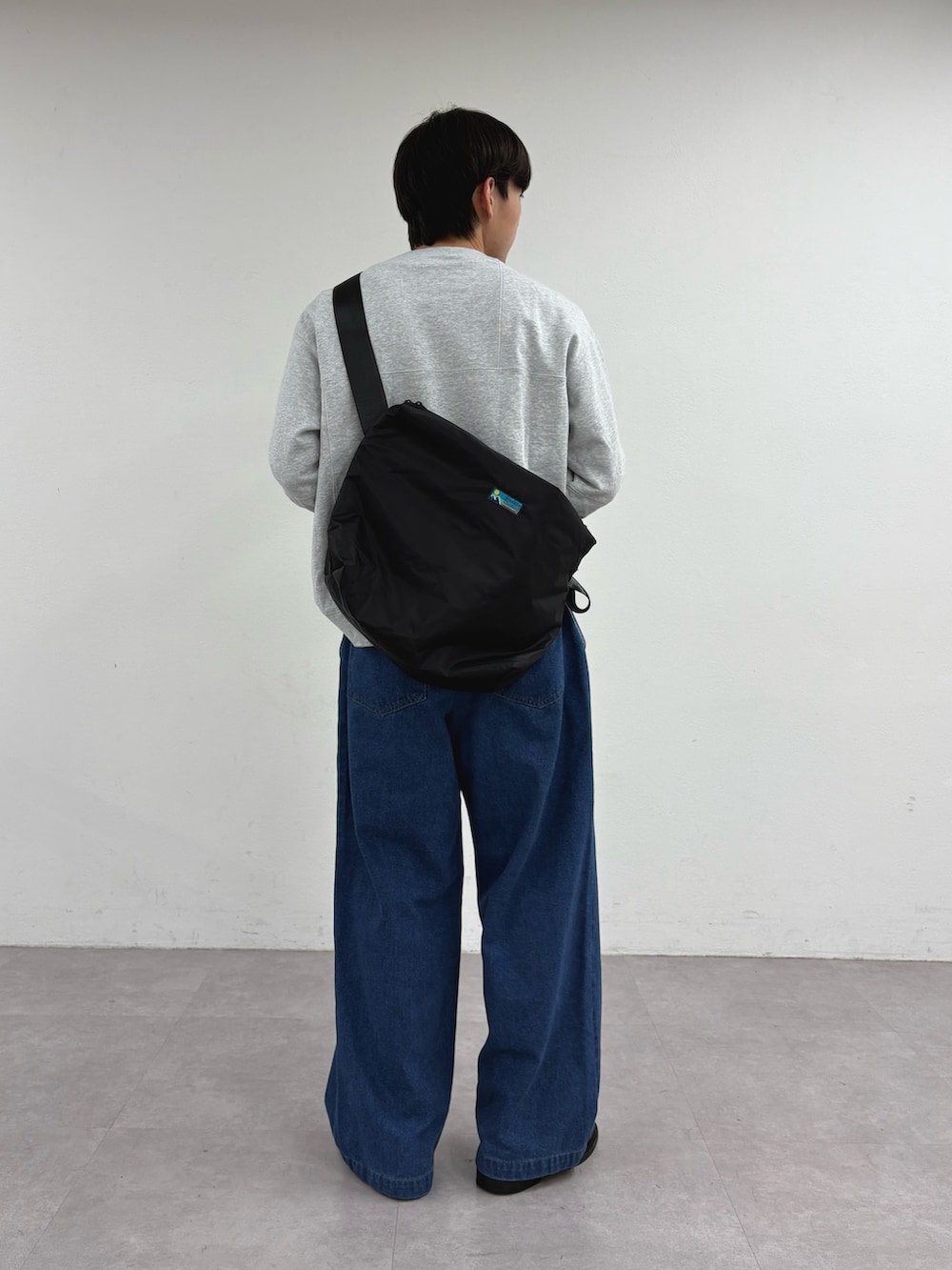 グレー系のスウェット、ブラック系のショルダーバッグ、ブルー系のデニムパンツを着用したメンズの冬コーディネートの2枚目の写真