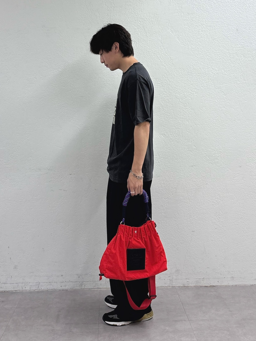 ブラック系のTシャツ/カットソー、ブラック系のスラックス、レッド系のトートバッグを着用したメンズの夏コーディネートの2枚目の写真