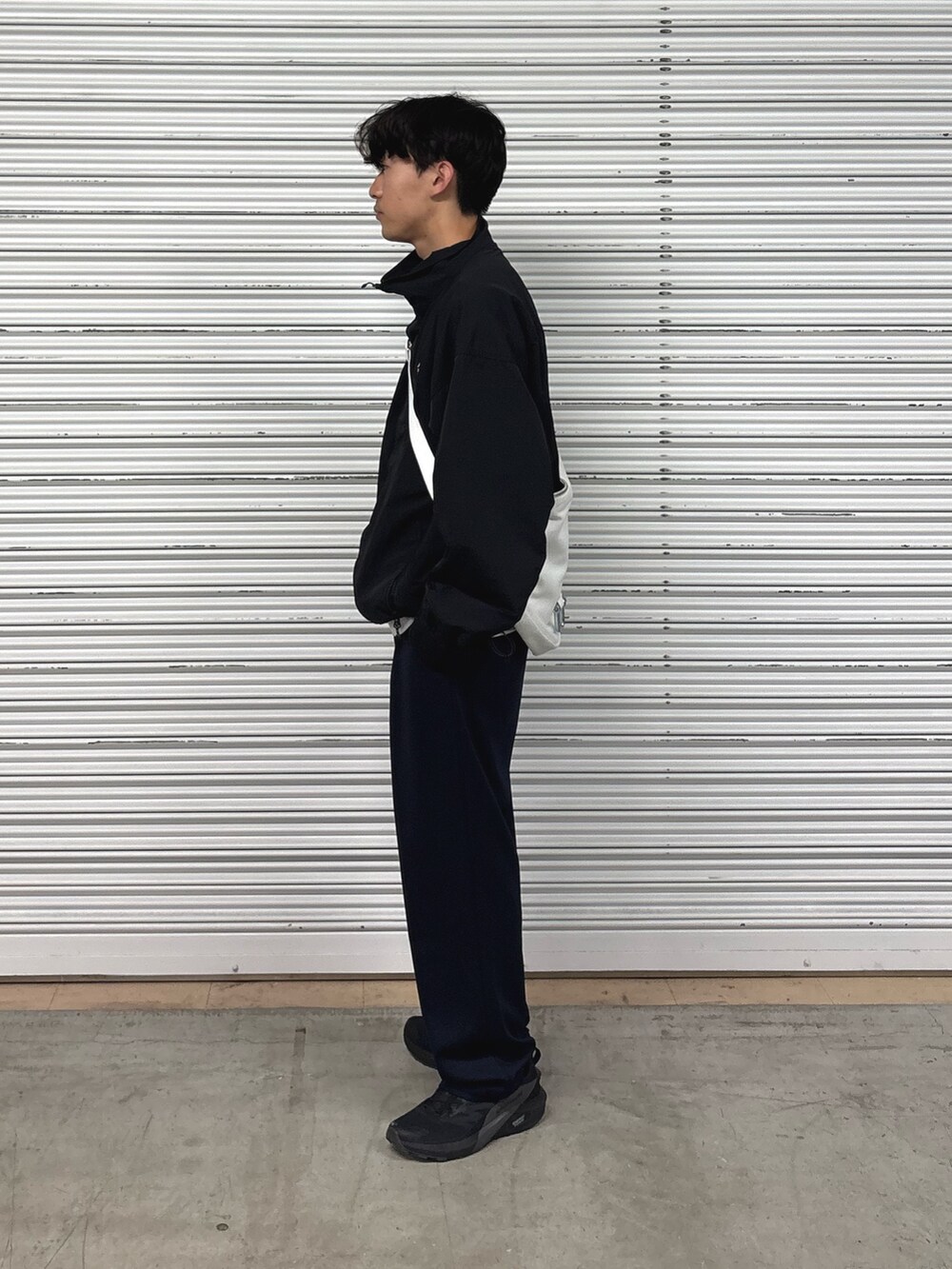 ブラック系のナイロンジャケット、ブルー系のスラックス、ホワイト系のショルダーバッグを着用したメンズの春コーディネートの2枚目の写真