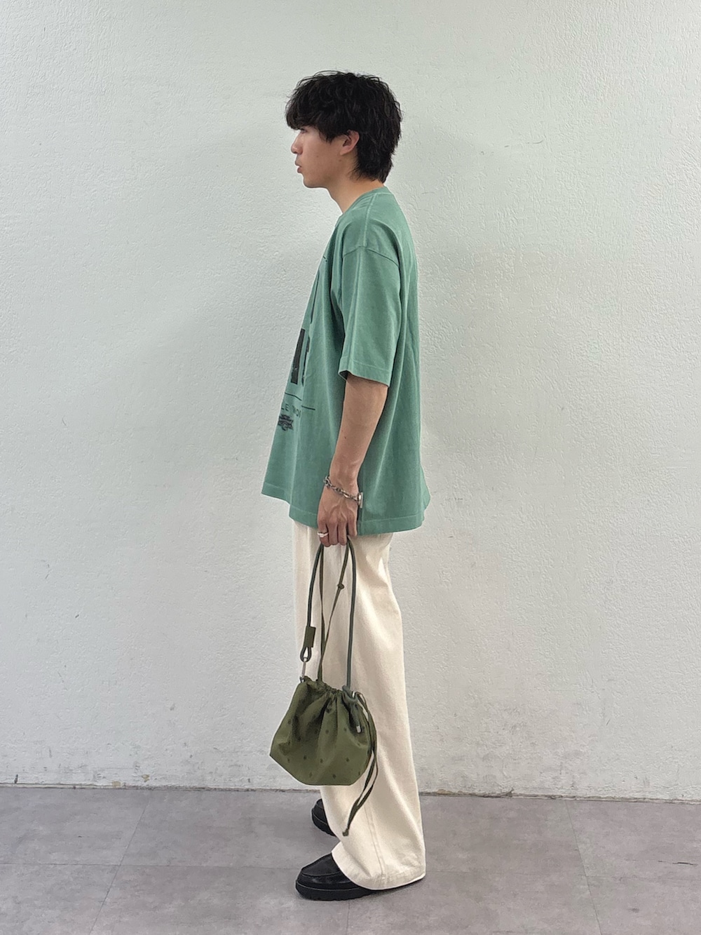 グリーン系のTシャツ/カットソー、グリーン系のショルダーバッグ、ホワイト系のデニムパンツを着用したメンズの春コーディネートの2枚目の写真