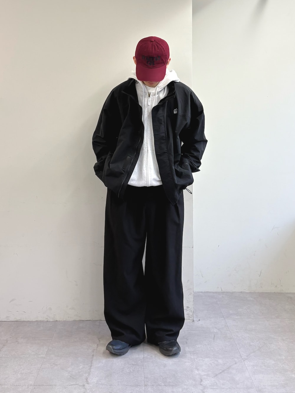 グレー系のパーカー、ブラック系のナイロンジャケット、ブラック系のスラックスを着用したメンズの春コーディネートの2枚目の写真