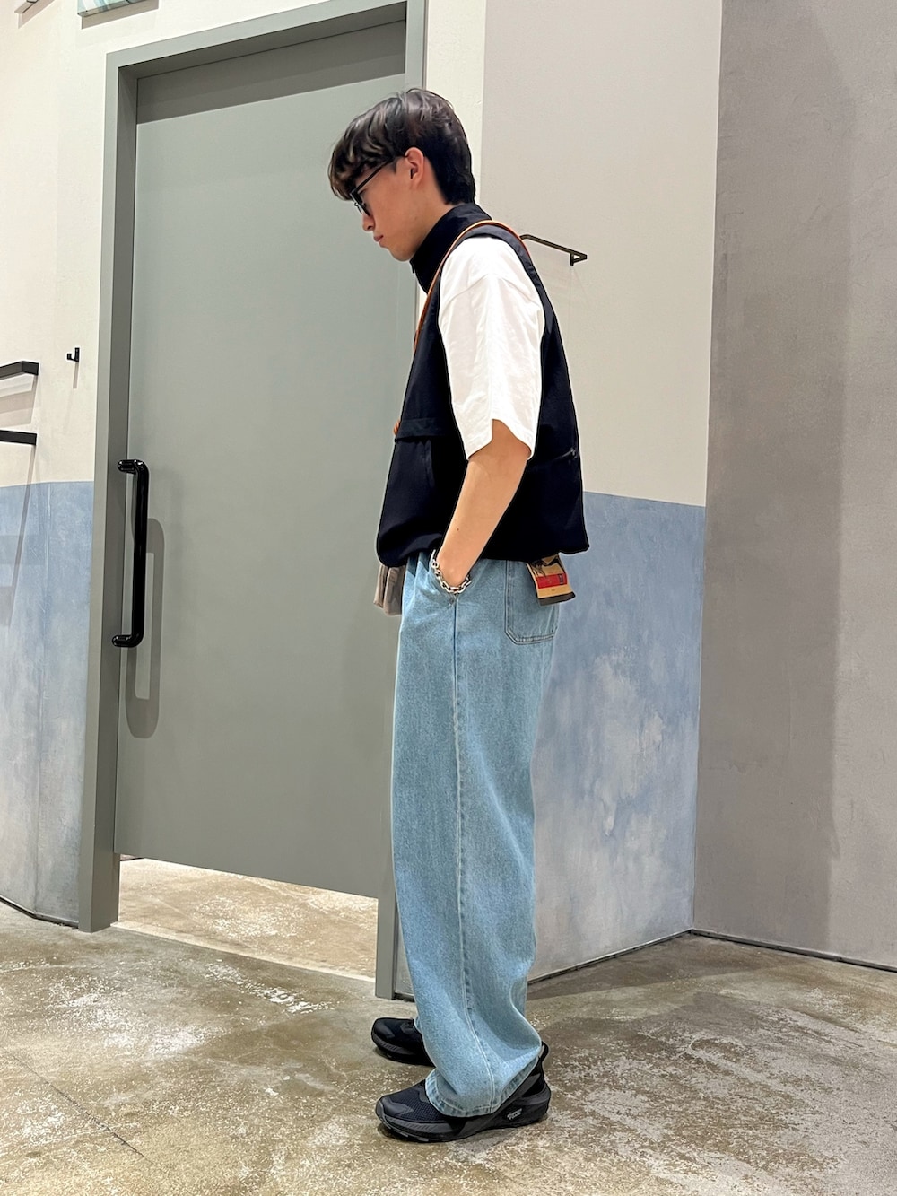 ブラック系のスニーカー、ブルー系のデニムパンツ、ブラック系のベストを着用したメンズの春コーディネートの2枚目の写真