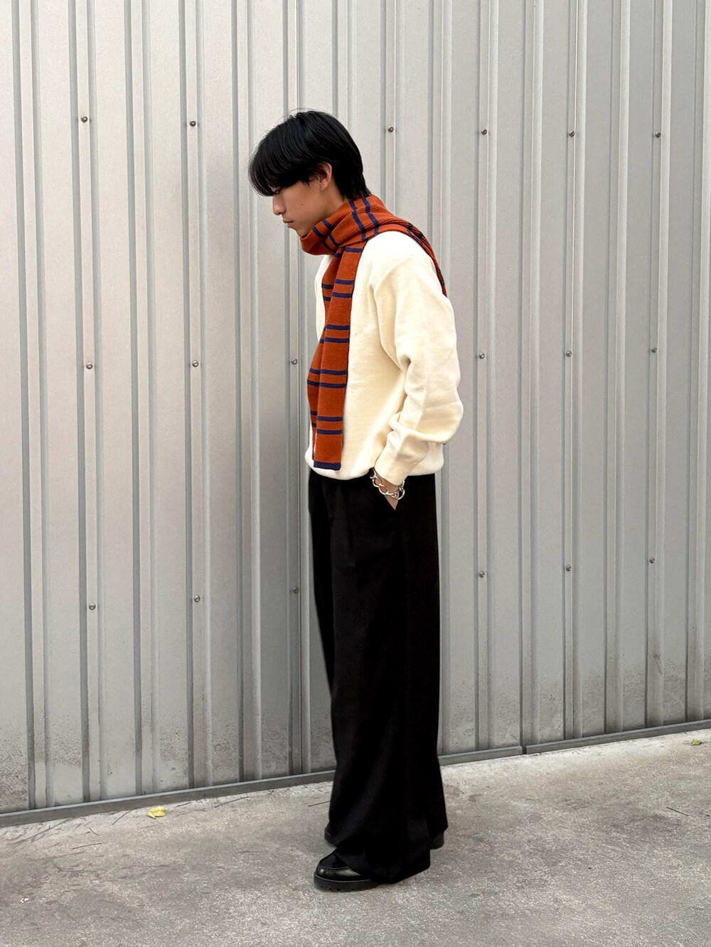 ブラック系のスラックス、ホワイト系のニット/セーター、オレンジ系のマフラーを着用したメンズの秋コーディネートの2枚目の写真