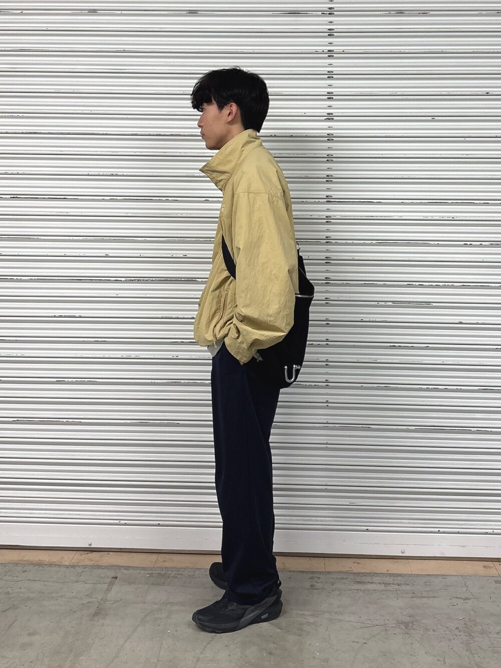 ベージュ系のナイロンジャケット、ブラック系のショルダーバッグ、ブラック系のスラックスを着用したメンズの夏コーディネートの2枚目の写真