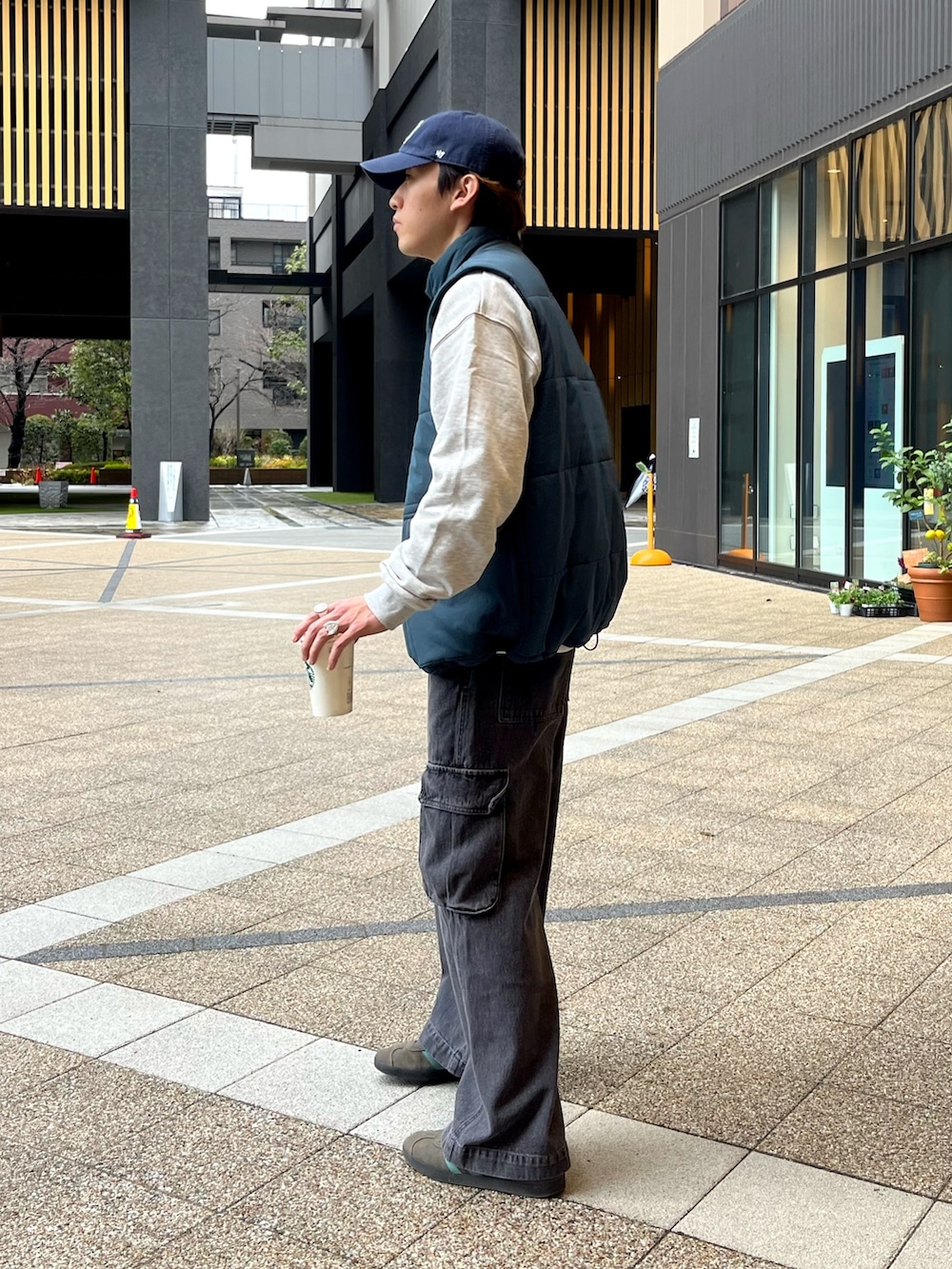 グレー系のスニーカー、ブラック系のカーゴパンツ、ブルー系のベストを着用したメンズの春コーディネートの2枚目の写真