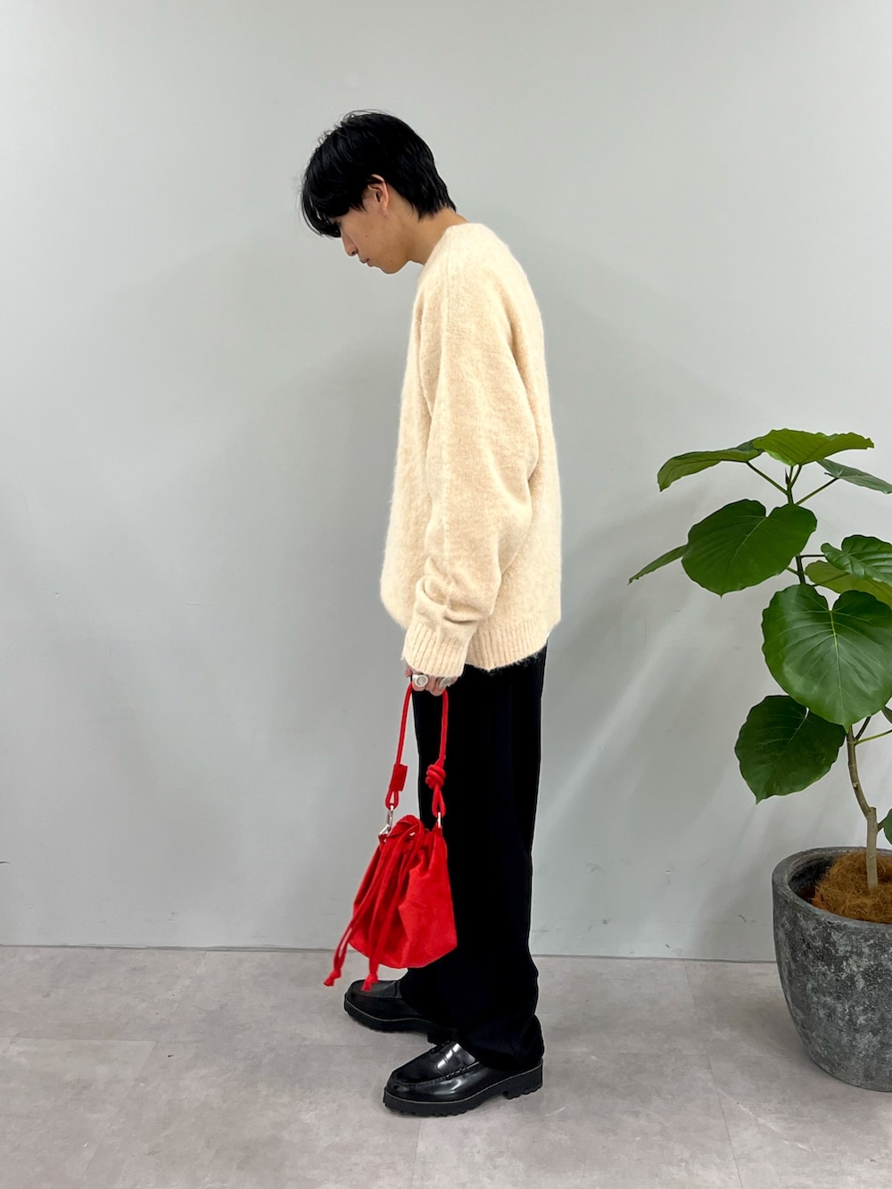 ホワイト系のニット/セーター、ブラック系のスラックス、レッド系のショルダーバッグを着用したメンズの冬コーディネートの2枚目の写真