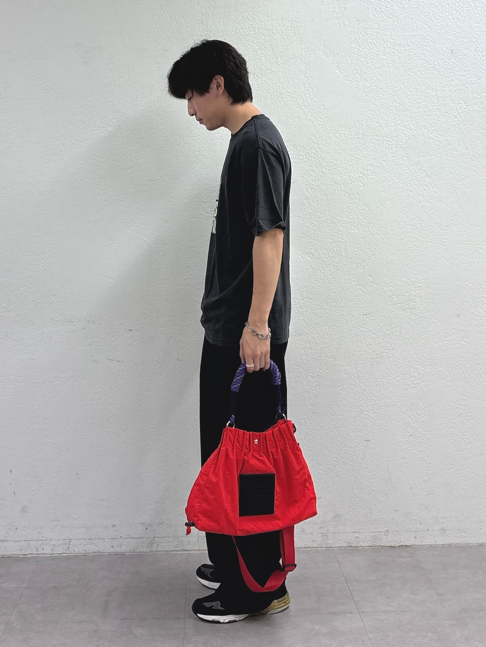 ブラック系のTシャツ/カットソー、ブラック系のスラックス、レッド系のトートバッグを着用したメンズの夏コーディネートの2枚目の写真