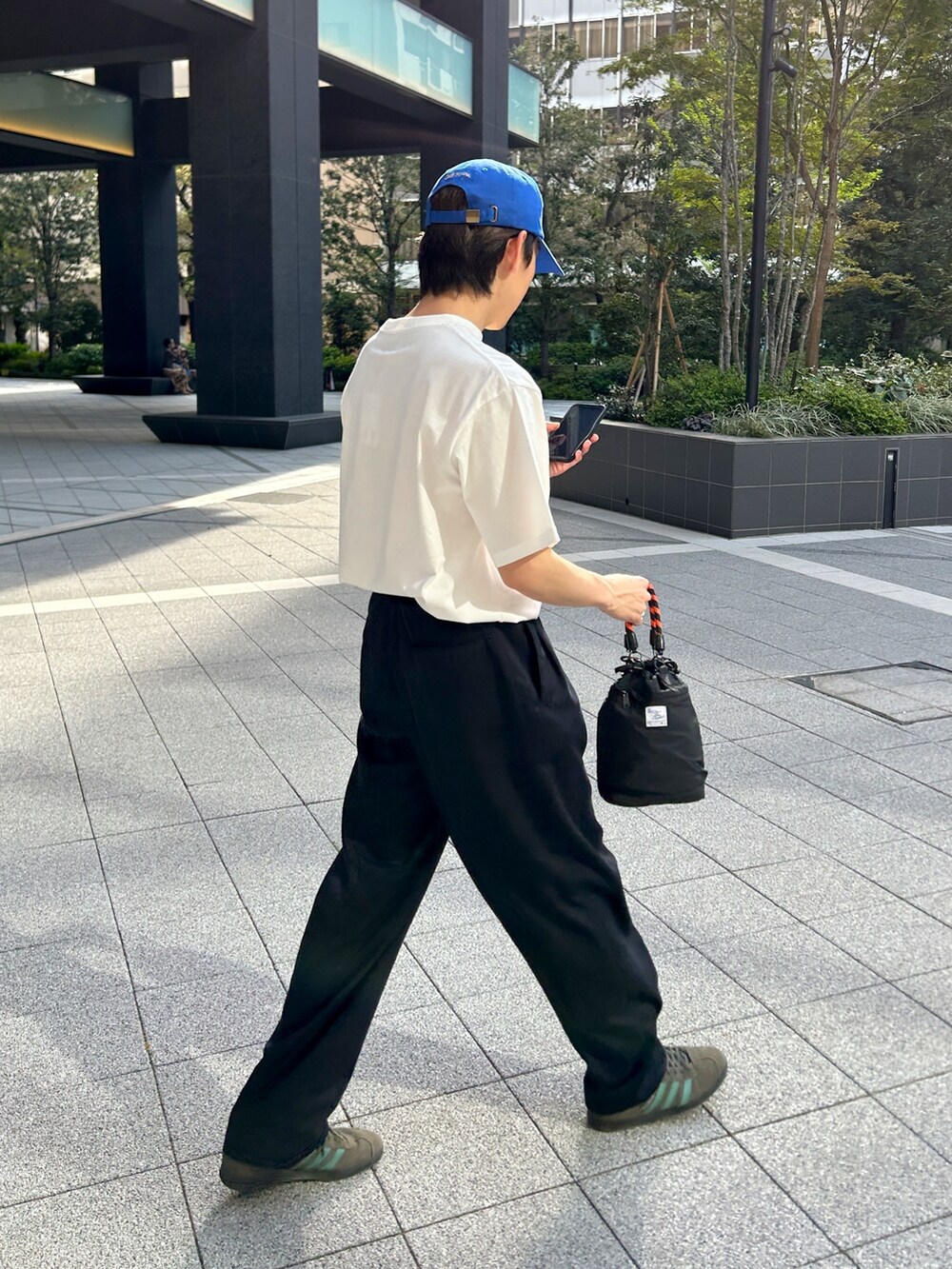 グレー系のスニーカー、ブラック系のスラックス、ブラック系のショルダーバッグを着用したメンズの春コーディネートの2枚目の写真