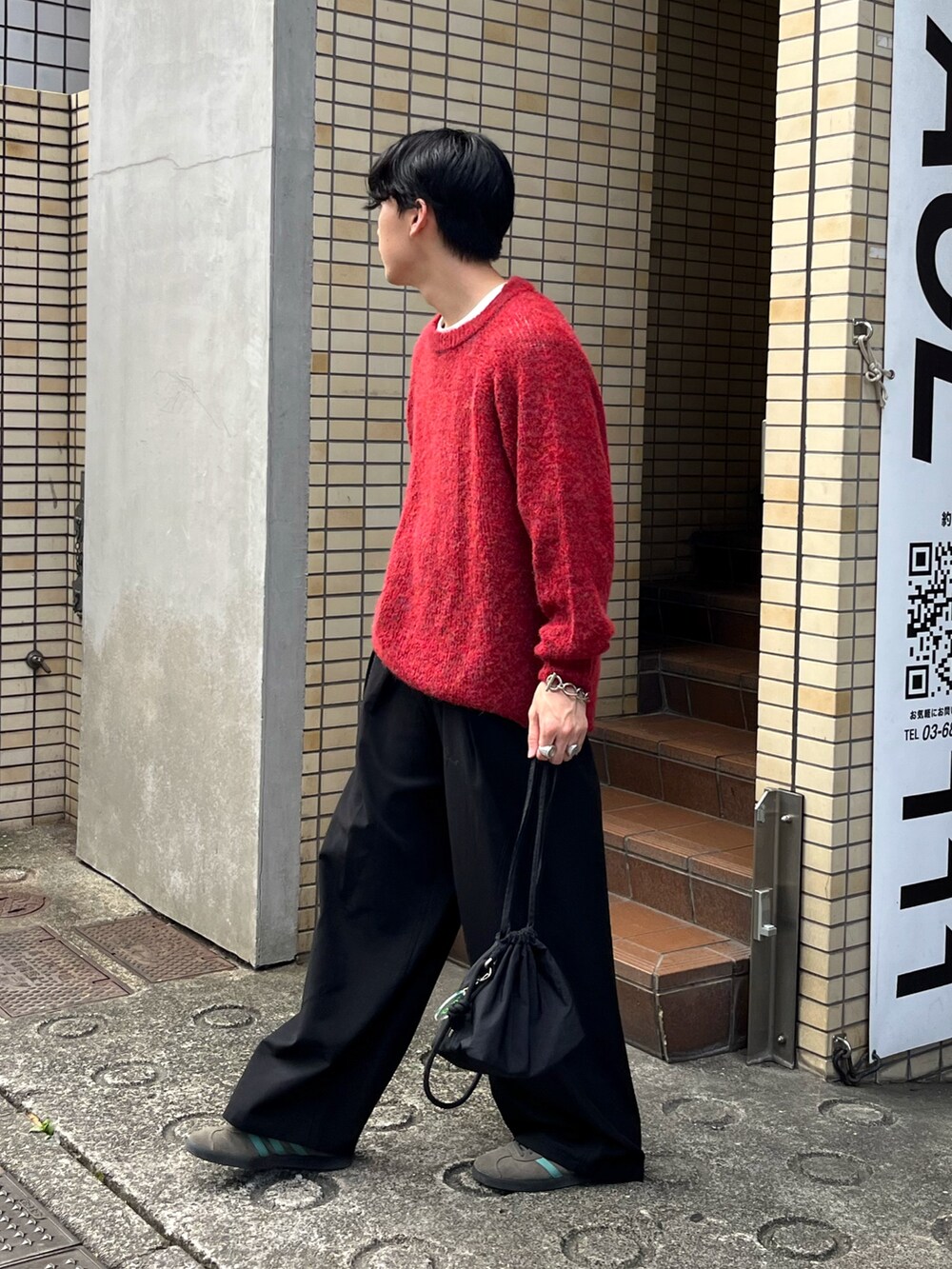 レッド系のニット/セーター、ブラック系のスラックス、ブラック系のショルダーバッグを着用したメンズの秋コーディネートの2枚目の写真