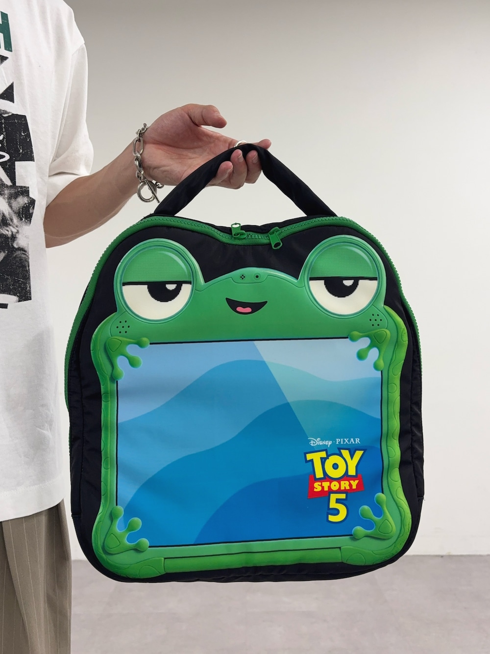 ホワイト系のTシャツ/カットソー、ベージュ系のスラックス、ブラック系のPC・タブレットケースを着用したメンズの春コーディネートの3枚目の写真