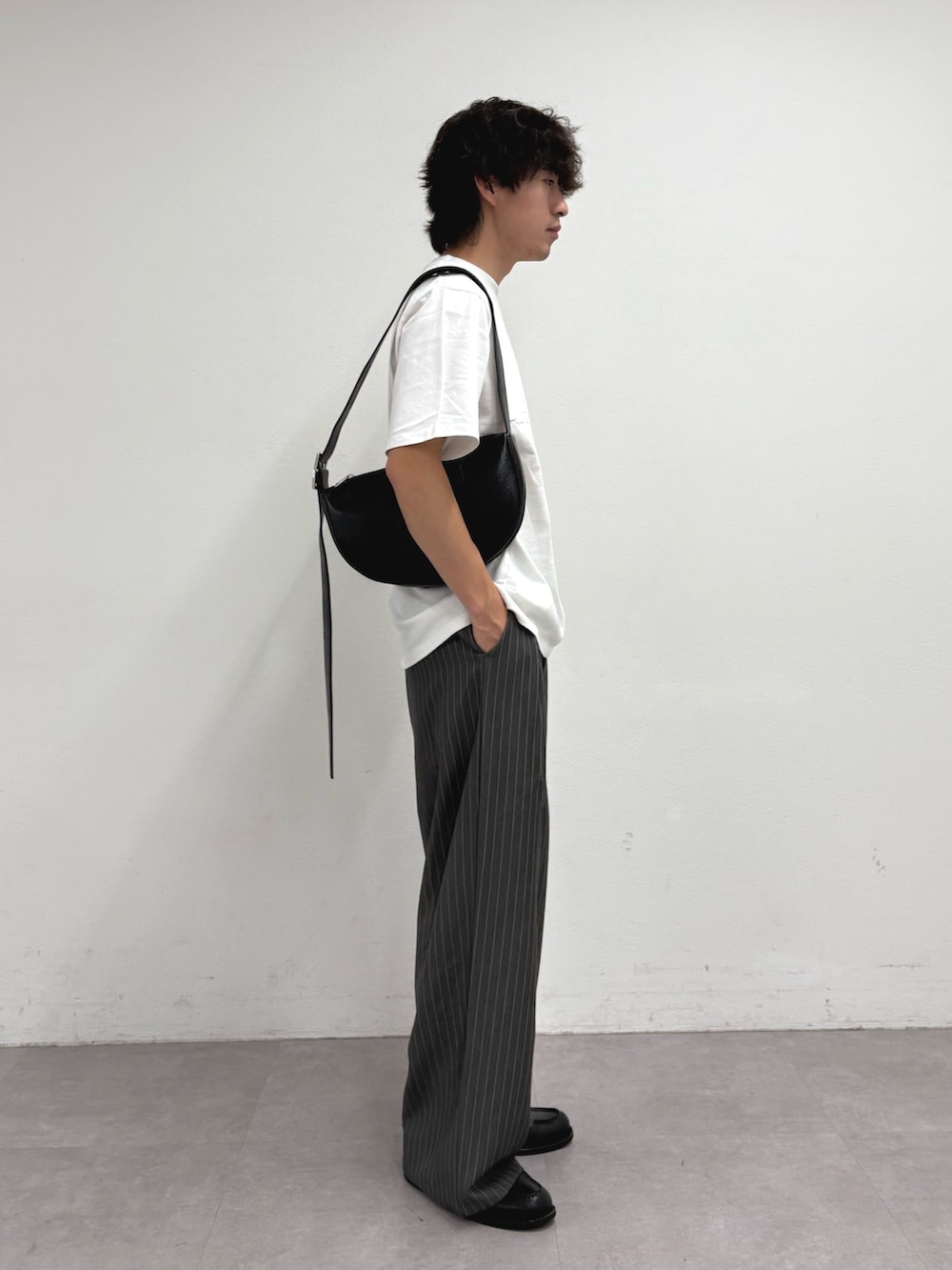 ホワイト系のTシャツ/カットソー、ブラック系のショルダーバッグ、グレー系のスラックスを着用したメンズの夏コーディネートの2枚目の写真