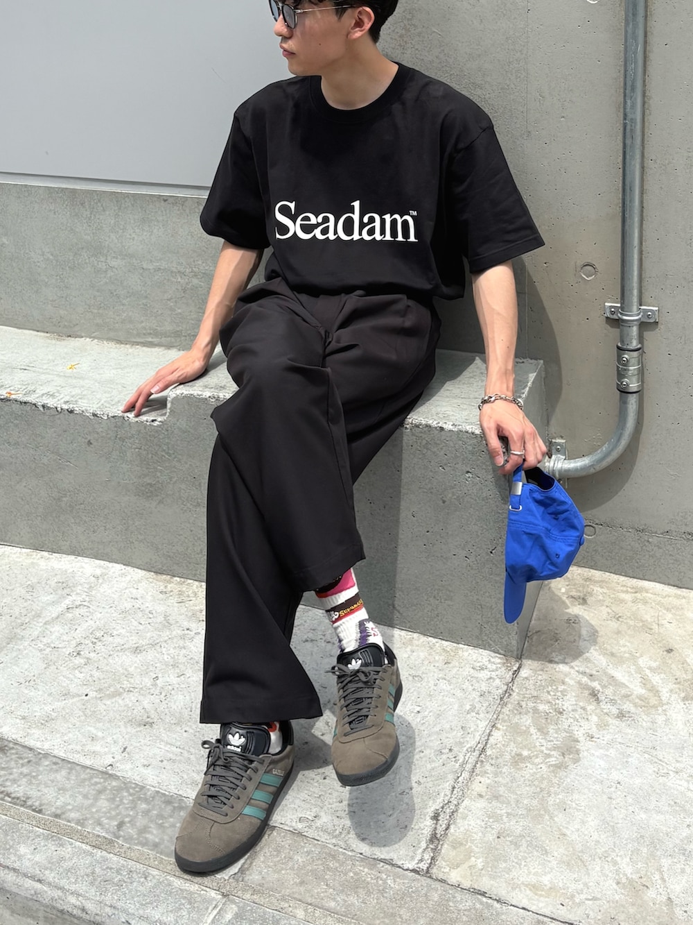 ブラック系のTシャツ/カットソー、ブラック系のスラックス、ブルー系のキャップを着用したメンズの春コーディネートの2枚目の写真