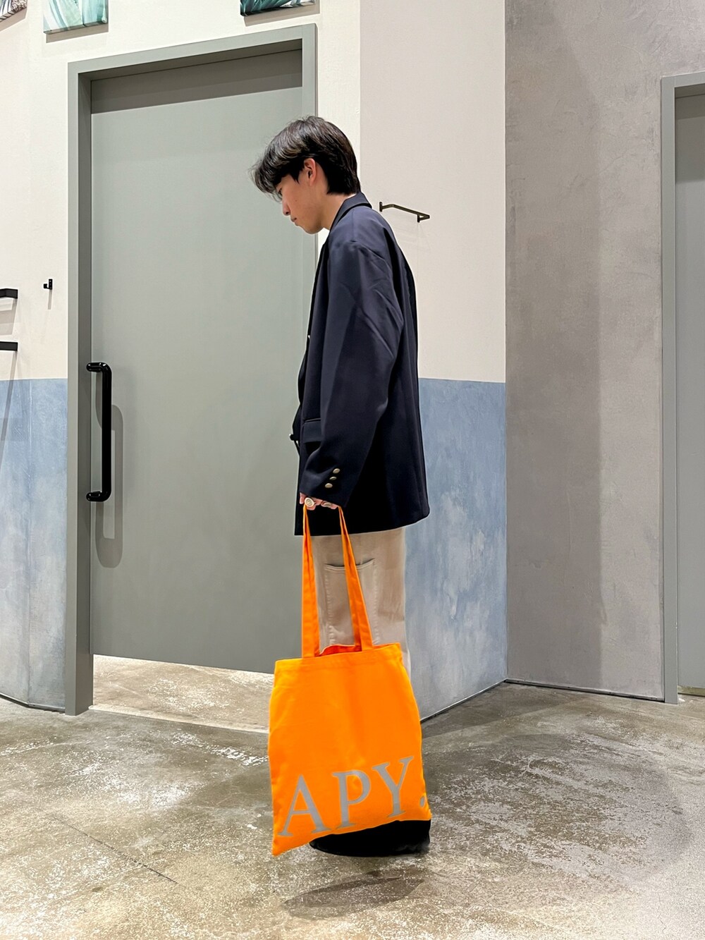 ブラック系のスニーカー、グレー系のデニムパンツ、オレンジ系のトートバッグを着用したメンズの春コーディネートの2枚目の写真