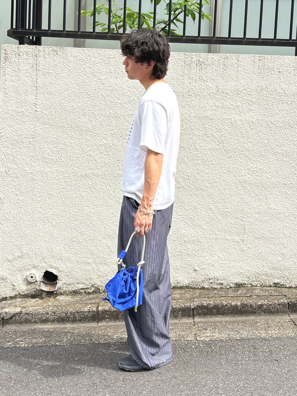 ホワイト系のTシャツ/カットソー、グレー系のスラックス、ブルー系のショルダーバッグを着用したメンズの夏コーディネートの2枚目の写真