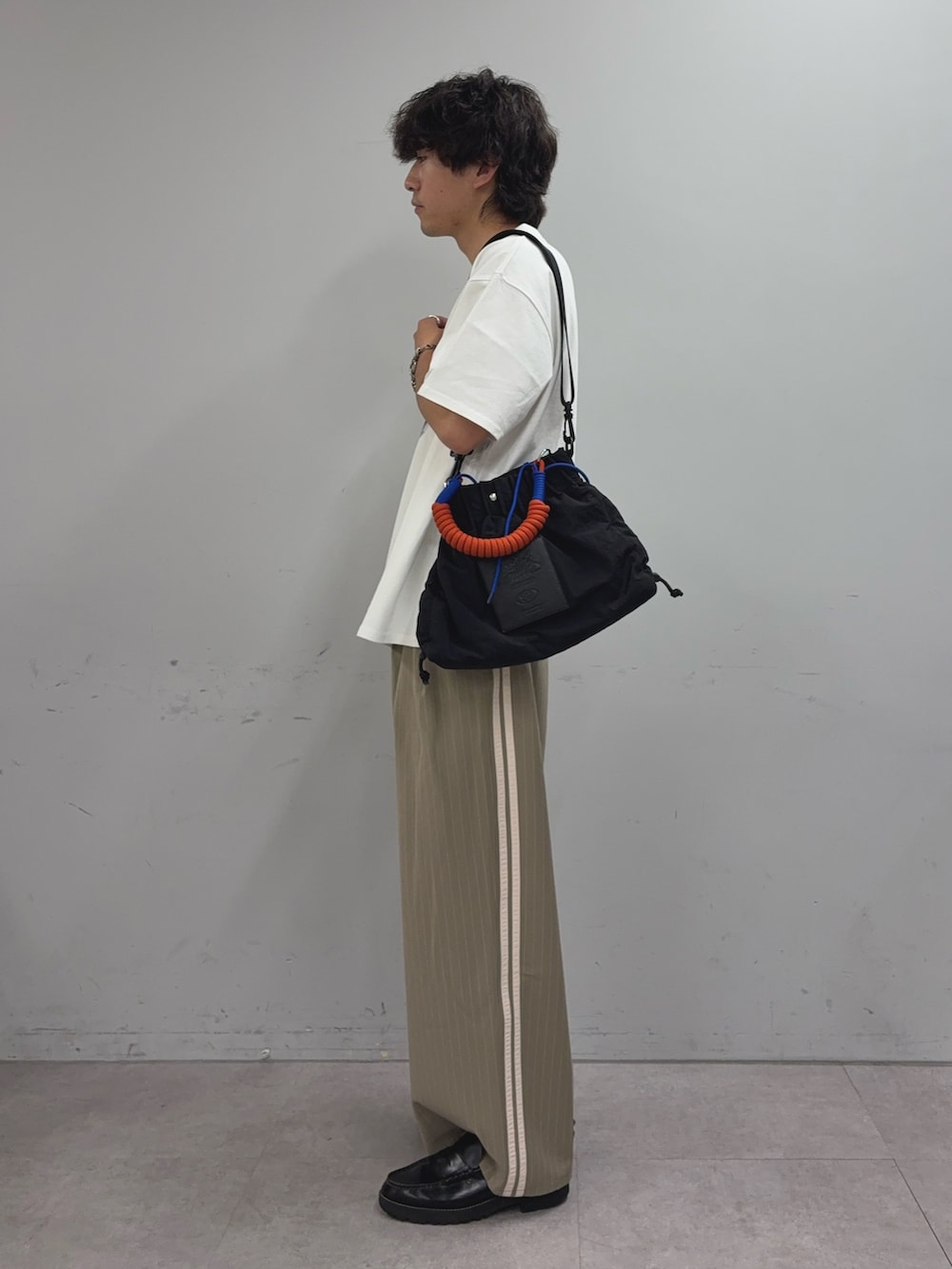 ホワイト系のTシャツ/カットソー、ベージュ系のスラックス、ブラック系のトートバッグを着用したメンズの夏コーディネートの2枚目の写真