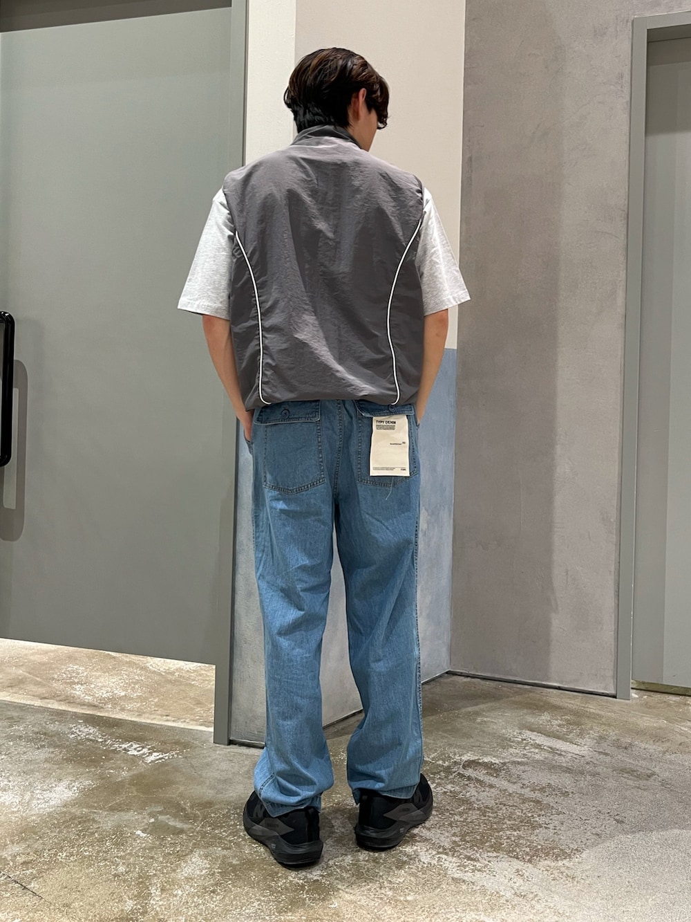 グレー系のベスト、ブラック系のスニーカー、ブルー系のデニムパンツを着用したメンズの夏コーディネートの2枚目の写真